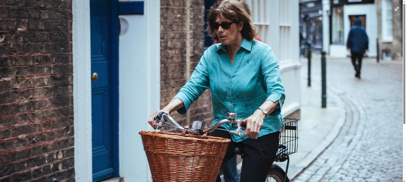 A woman cycling with a wicker shopping basket on a cobbled UK street